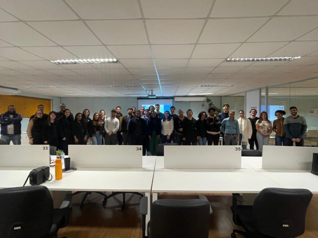 O palestrante e o público posam juntos para uma foto em frente à sala, reunidos em grupo e olhando para a câmera.